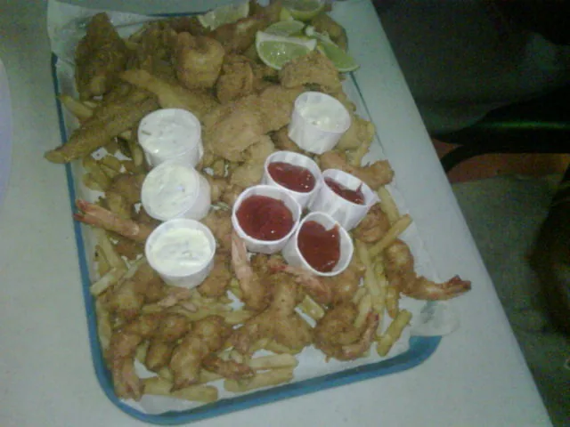 A platter of fried shrimp, fish and fries with cups of sauce